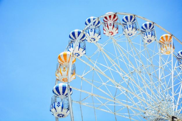 Front view of half retro colorful ferris wheel at amusement park over blue sky background