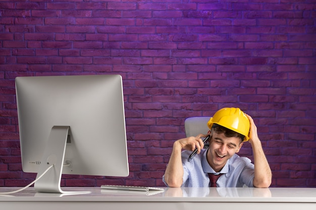 Front view happy male constructor behind office desk talking at phone