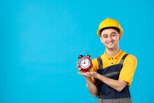 Front view of happy male worker in uniform with clocks on blue wall