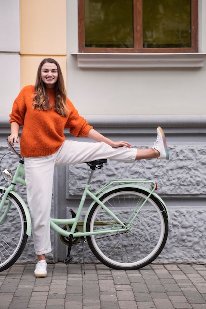 Front view of happy woman posing with her bicycle outside