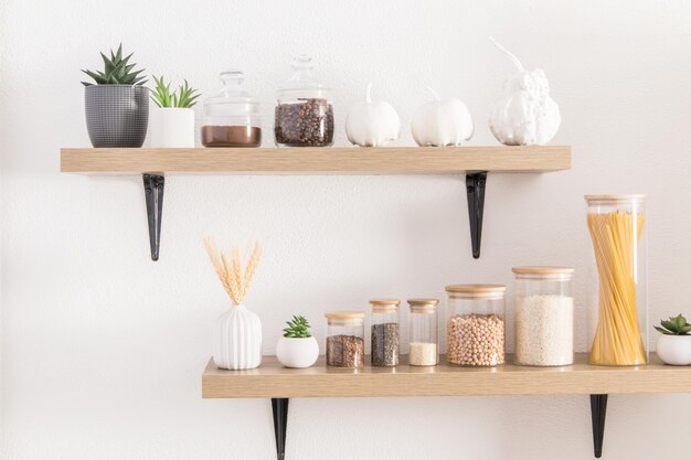 Front view of the kitchen shelves with various ecojars for storing bulk products front view white wall cactus in pots