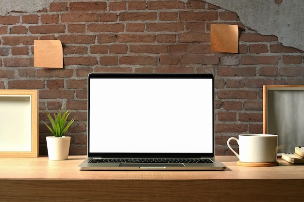 Front view of laptop computer with blank screen houseplant coffee cup and books on wooden table