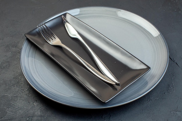 Front view long black plate with fork and knife in gray plate on dark