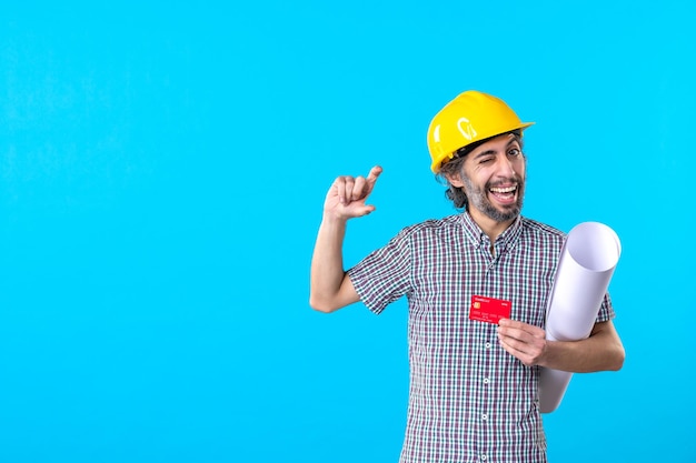 Front view male builder holding plan and bank card on blue background color constructor job architecture building