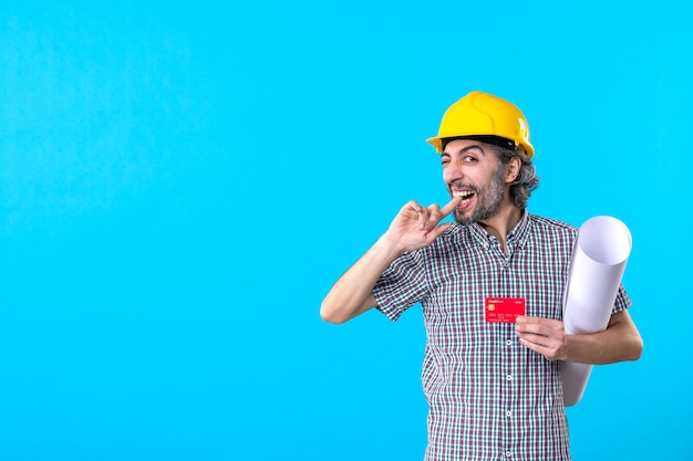 Front view male builder holding plan and bank card on blue background money design constructor architecture building job work color