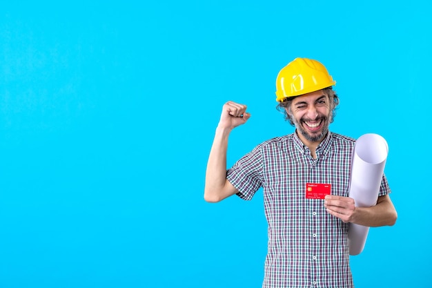 Front view male builder holding plan and bank card on blue background money design constructor job work colors architecture building