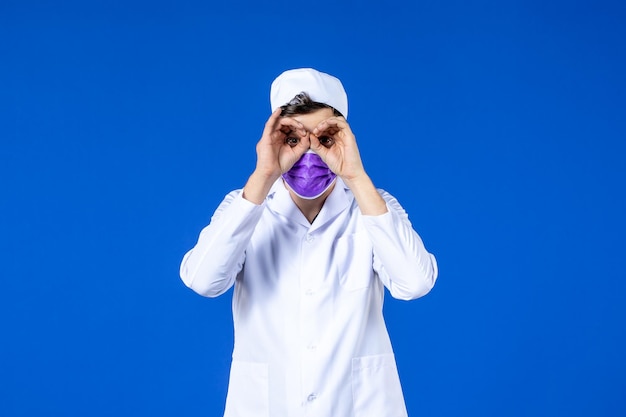 Front view of male doctor in medical suit and purple mask on blue 