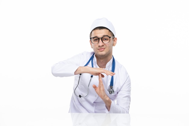 Front view male doctor in medical suit sitting behind desk