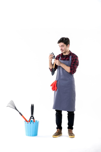 front view male gardener holding little spatulas on white background soil work green tree flower garden ground uniform