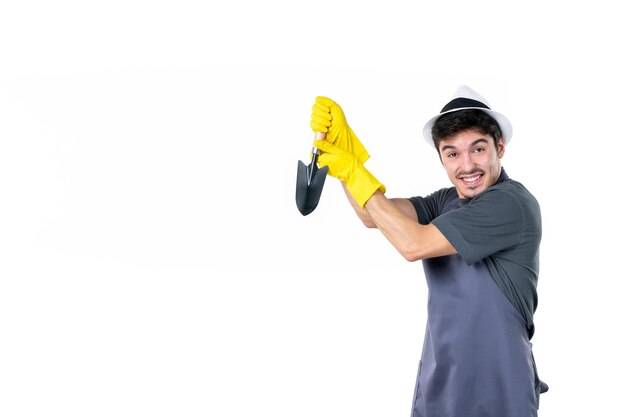 Front view male gardener in yellow gloves holding little spatula on white background tree flower garden ground work bush grass job