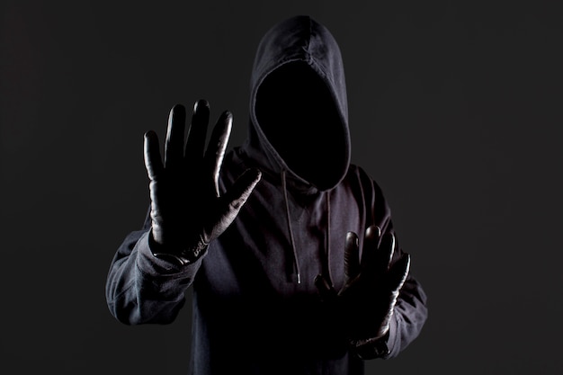 Front view of male hacker with gloves holding hand up as stop