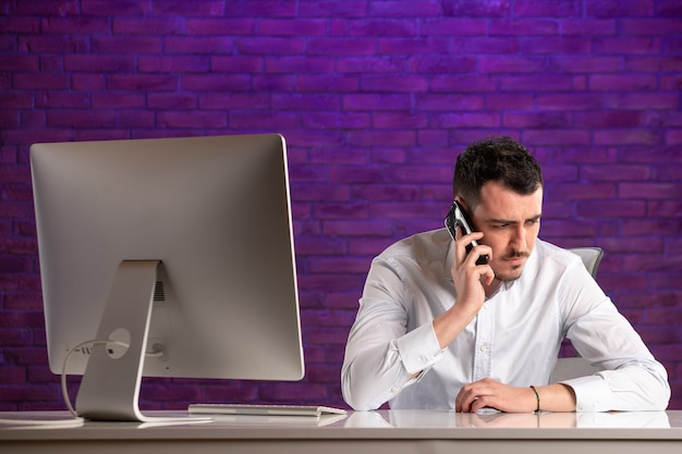 Front view male office worker sitting behind his working place talking