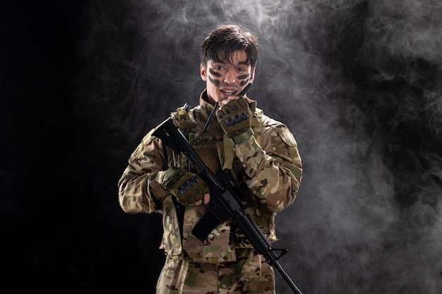 Front view of male soldier with machine gun using walkie-talkie black wall