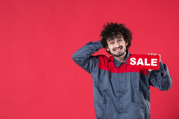 Front view male worker holding red sale nameplate on red background mechanic photo house color shopping job uniform instrument