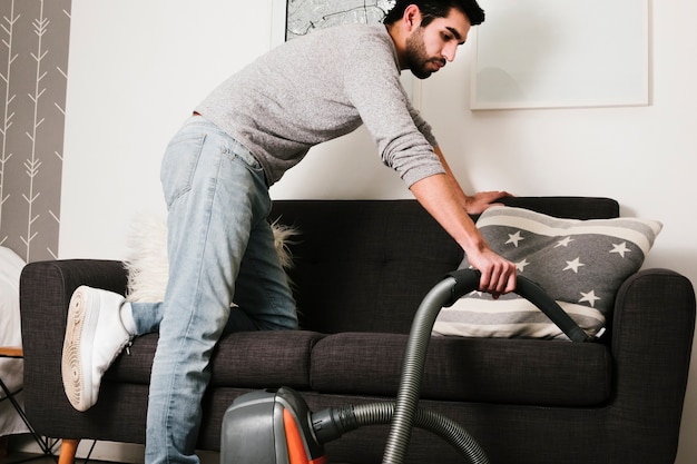 Front view man vacuuming couch