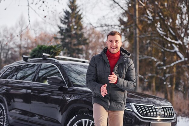 Photo front view man with little green fir is outdoors near his car conception of holidays