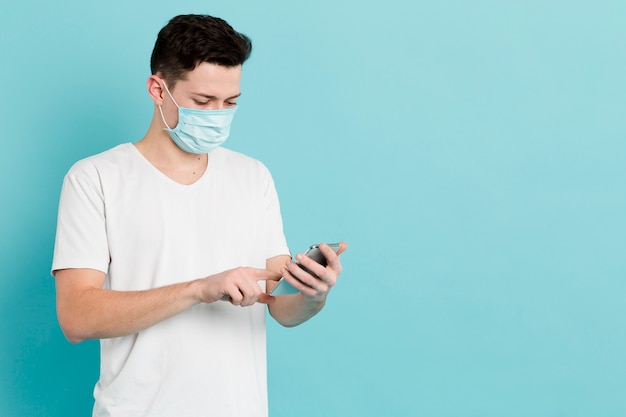 Front view of man with medical mask looking at smartphone