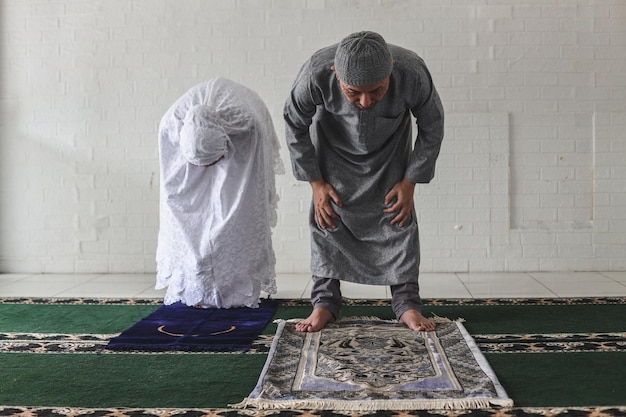 Front view of muslim couple wearing praying salah together in mosque doing ruku movement kneeling