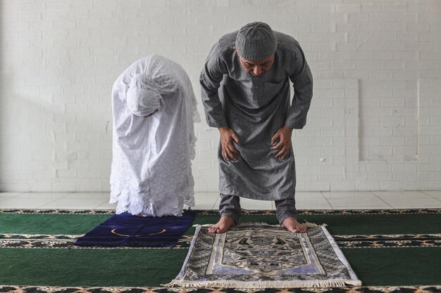 Photo front view of muslim couple wearing praying salah together in mosque doing ruku movement kneeling