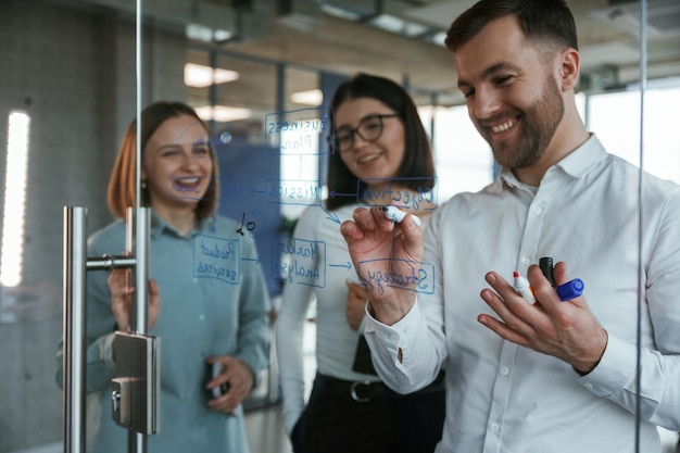 Front view Office workers are creating plan standing by glass and writing on it