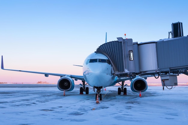 Front view of the passenger jet plane near the boarding bridge at winter airport apron