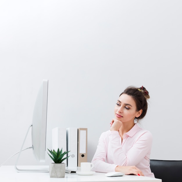 Front view of pensive woman at her desk looking at computer