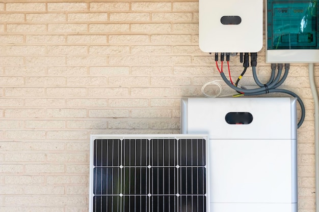 Front view of photovoltaic panel and battery instalation leaning on the beige white wall