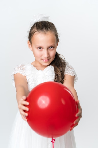 Front view of playful girl holding out red balloon with both hands and looking at camera