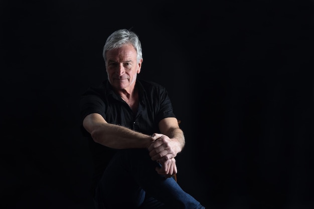 Front view portrait of senior man sitting on chair on black background