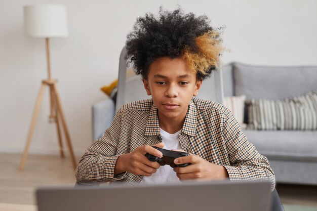 Front view portrait of teenage African-American boy holding gamepad while playing videogames at home, copy space