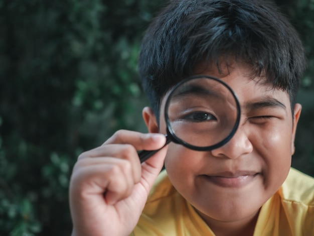 Front view portrait of a young asian child holding a magnifying glass for reading in hand inspecting Investigating to have close look with eye in focus