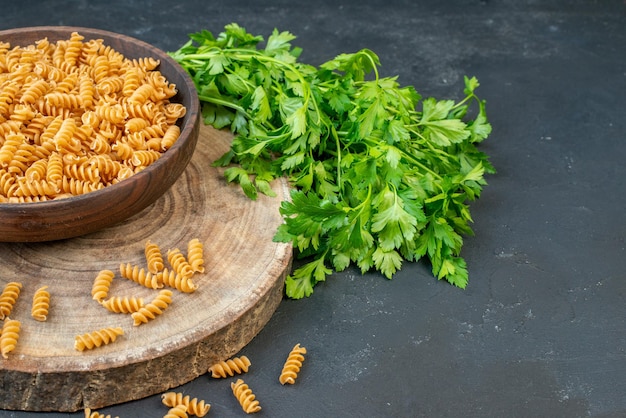 Front view of raw pastas inside and outside brown pot green bundle on dark blue color background