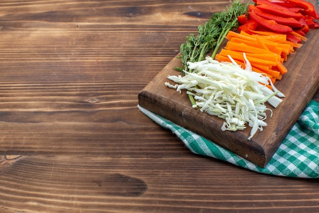 Front view sliced vegetables cabbage carrot greens and pepper on cutting board brown surface