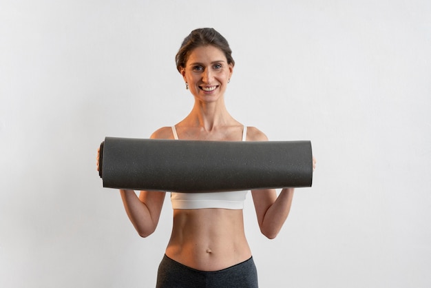 Front view of smiley woman holding yoga mat