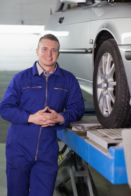 Front view of a smiling mechanic next to a car