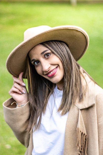 Front view of a smiling young brunette woman with her hand on her hat at sunset in the nature vertical portrait