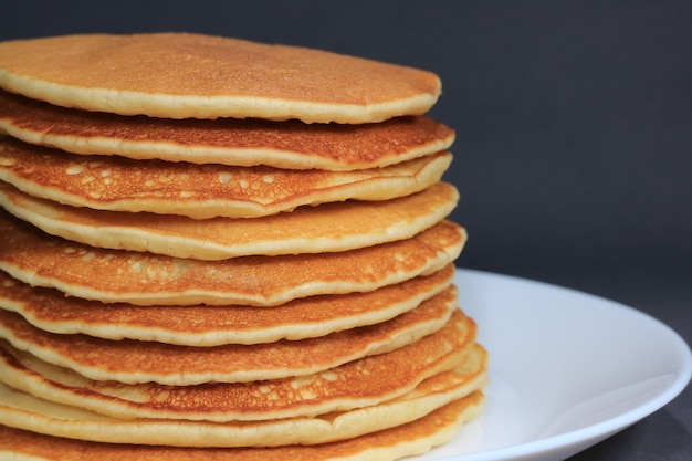 Front view of Stack of homemade plain pancakes served on white plate on black background