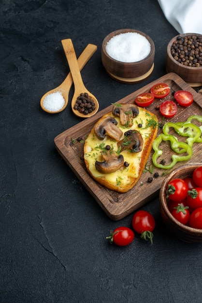 Front view of tasty snack with mushrooms and chopped vegetables on wooden board cutlery set spices on black background