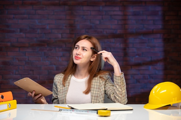 front view thinking female worker in construction site sitting behind table with documents job corporate plan manager engineer project agenda planner business