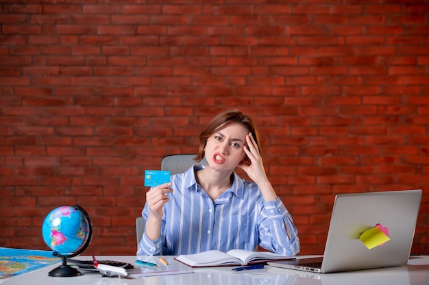 Front view travel agent behind her working place holding credit card map indoors manager worker service agency document operator world money