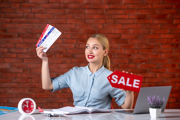 front view of travel agent sitting behind her working place holding tickets and sale nameplate assistant global manager indoors occupation tourism agency