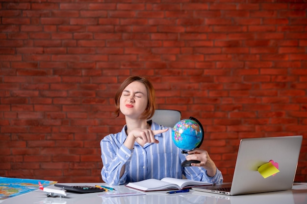 Front view travel agent sitting behind her working place with little globe map assistant agency service world manager operator