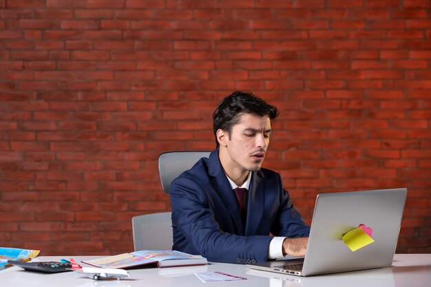 front view of travel agent sitting behind his working place in suit and using laptop corporate occupation tourism overseas project service global agency assistants