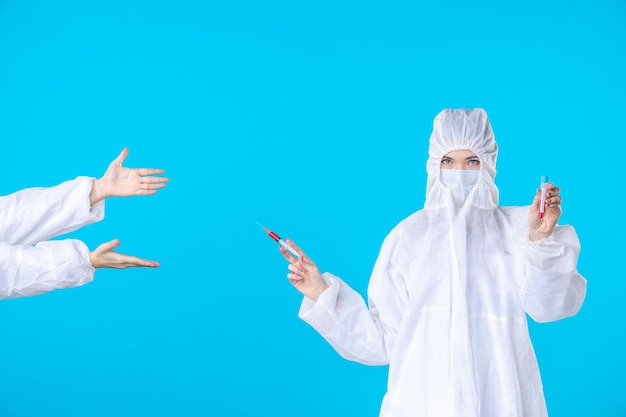 front view two female doctors in protective suit and mask one holding injection on a blue background medical covid- virus health science hospital pandemic