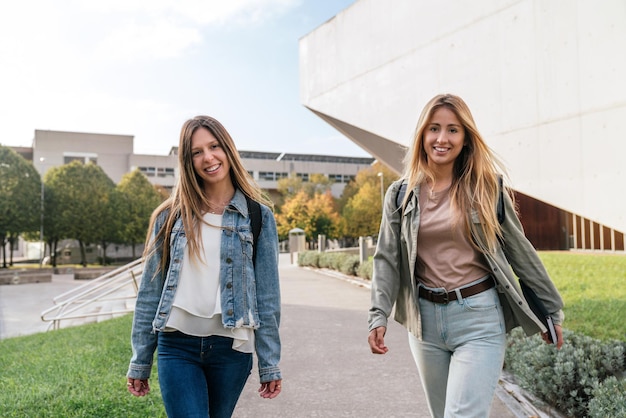 Front view of two female university colleagues walking around campus looking at camera.