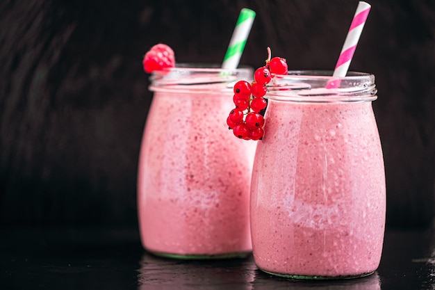 Front view of two jars with yogurt pink smoothie with cranberry raspberry on black background