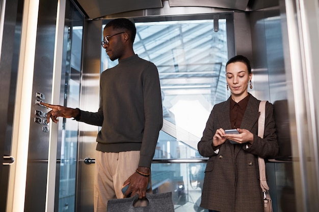 Front view of two young business people in glass elevator at modern office building copy space