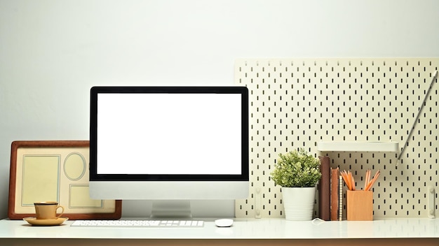 Front view of white blank screen computer monitor picture frame pencil holder and houseplant on working table