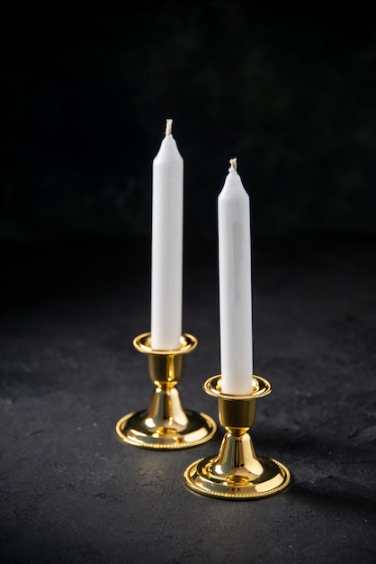 Front view of white candle in golden stand on black