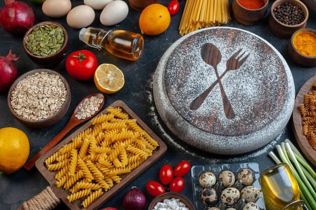 Front view white flour in fork and spoon shape around eggs tomatoes seasonings and pasta on dark background color dough vegetables meal food